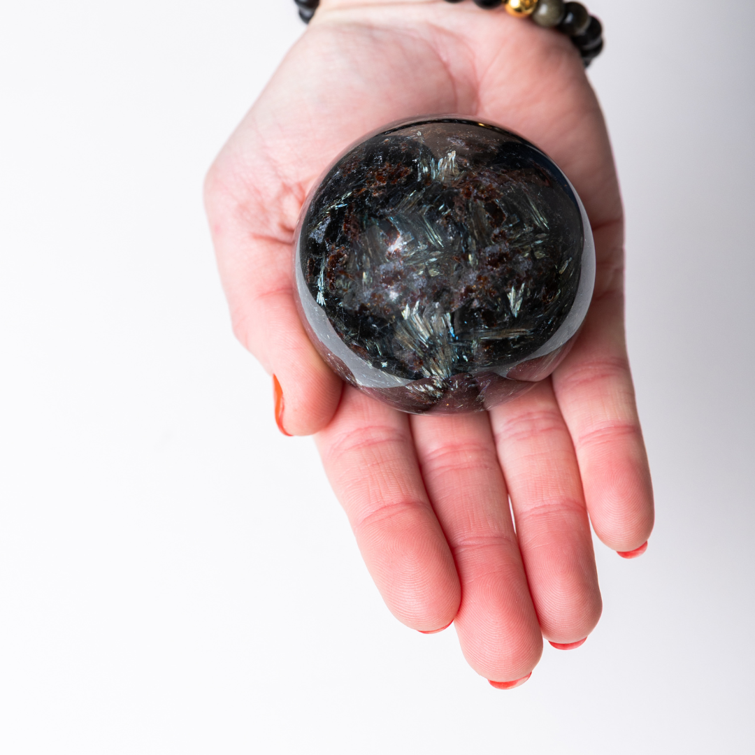Hand holding a dark crystal ball against a white background