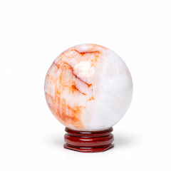 A polished white marble crystal sphere with orange and reddish-brown veining, displayed on a dark reddish-brown wooden stand against a white background.