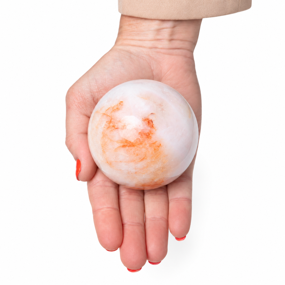 A hand holding a polished white stone sphere with orange and peach marbled patterns, shown against a plain white background.