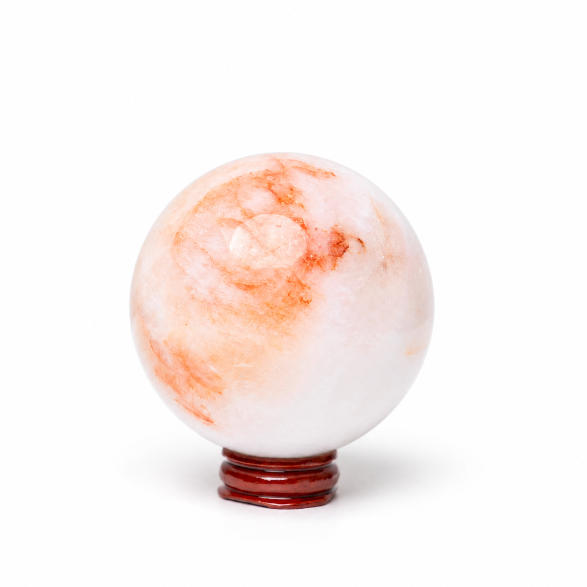 A polished white stone sphere with soft orange and peach marbling, displayed on a small dark reddish-brown stand against a clean white background.