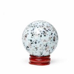 A polished crystal sphere with a light blue and white base speckled with black, gray, and brown flecks, displayed on a small red wooden stand against a plain white background.