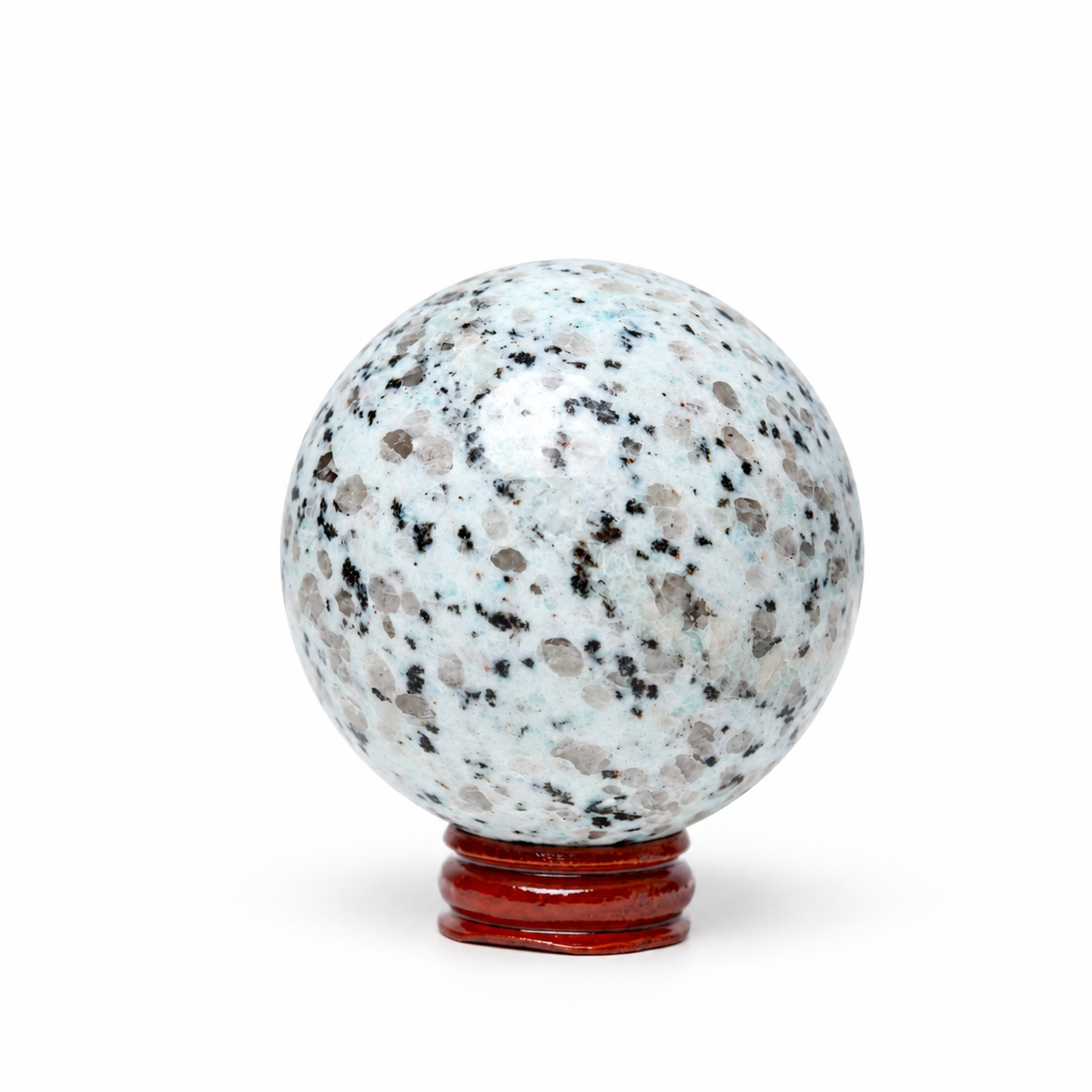 A polished crystal sphere with a white and light blue base speckled with black, gray, and brown flecks, displayed on a small reddish-brown wooden stand against a plain white background.