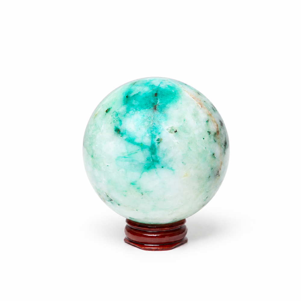 A polished jadeite crystal sphere with green and turquoise marbling, displayed on a small dark reddish-brown wooden stand against a plain white background.