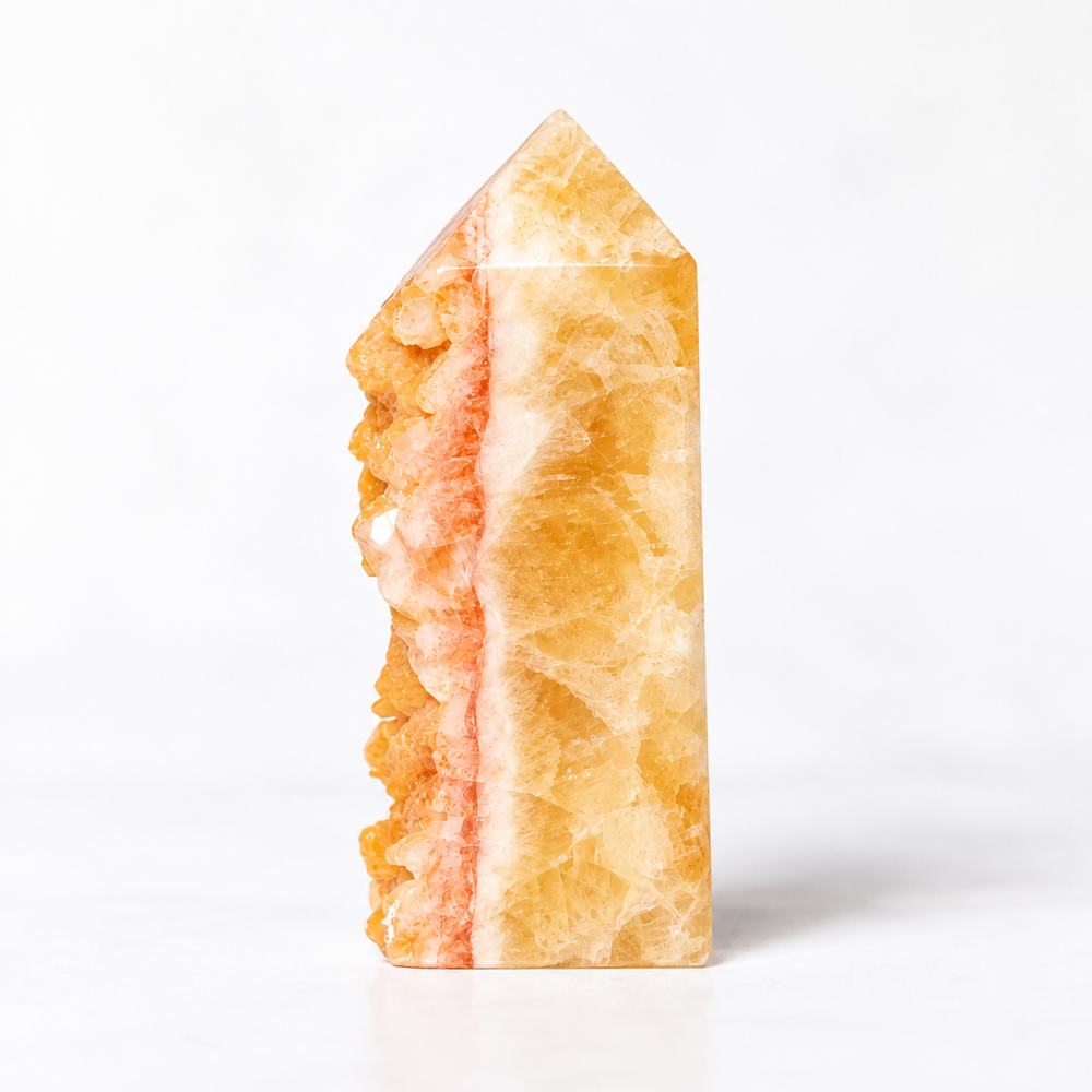 A polished natural crystal point with a pointed top, featuring a translucent golden-yellow body with a prominent pinkish-orange textured edge, photographed on a seamless white background.
