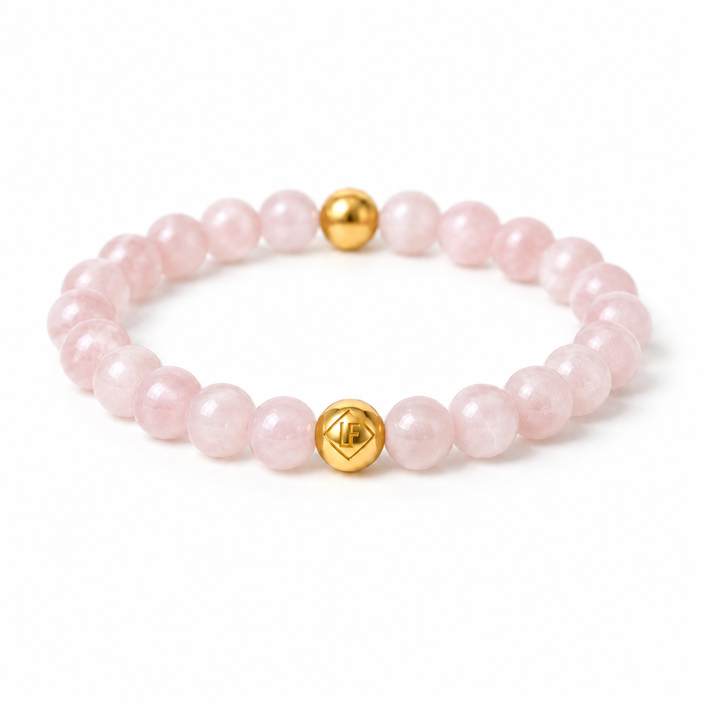 A pink stone beaded bracelet with two polished gold accent beads, one featuring a geometric symbol, displayed on a clean white background.
