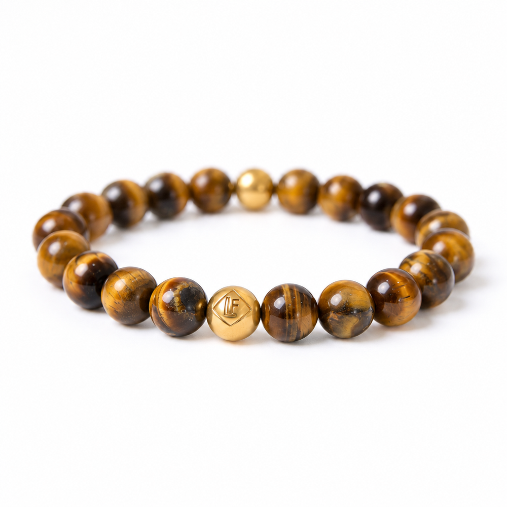 A beaded stretch bracelet made of polished brown and black tiger's eye beads, featuring a central gold 18k plated bead engraved with a geometric symbol, shown on a plain white background.
