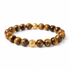 A beaded stretch bracelet made of polished brown and black tiger's eye beads, featuring a central gold 18k plated bead engraved with a geometric symbol, shown on a plain white background.